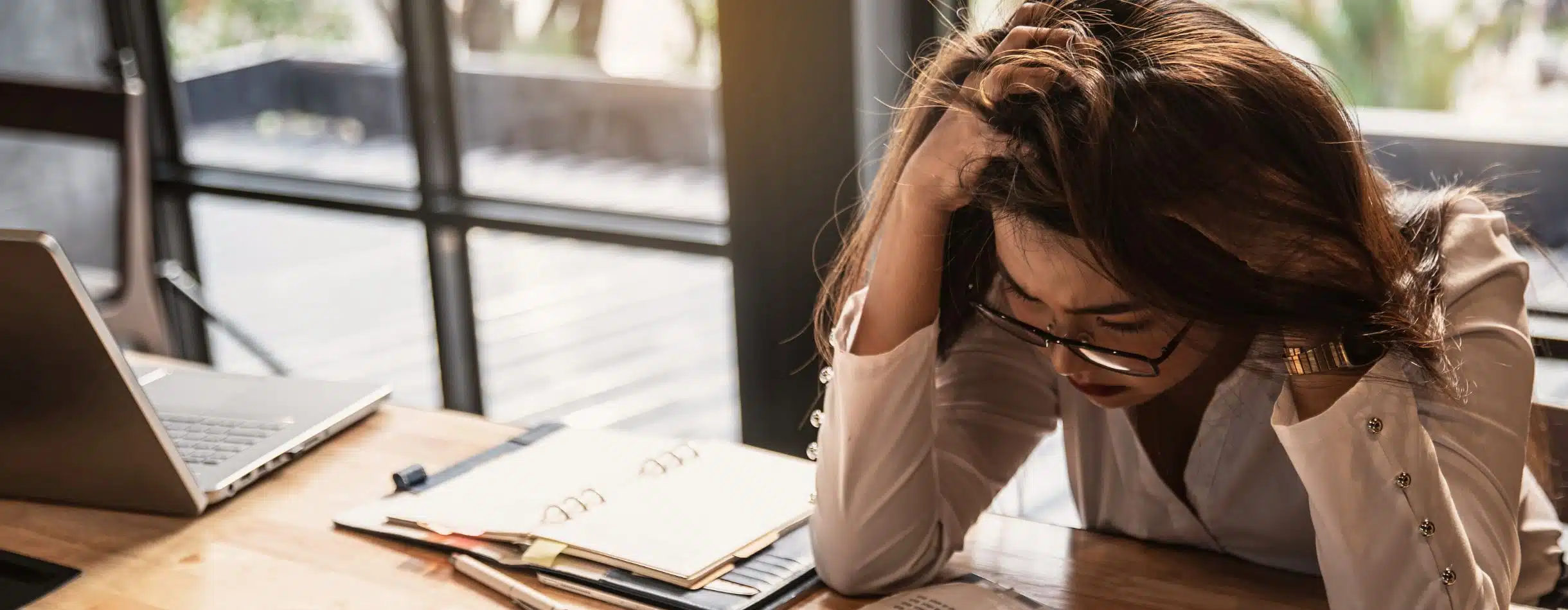 In a moment of pure frustration, a woman grabs the top of her head, slightly tugging at her hair. The other hand is resting on the back of her neck, likely as a response to mildly calm herself down as the data set she's working with is full of errors and miscalculated formulas.
