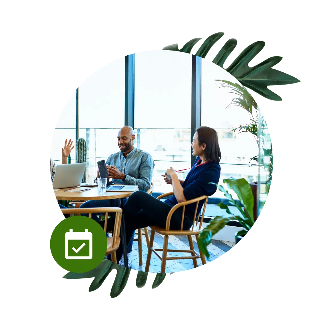 A man and woman discuss ideas at a table, sharing a laugh about a joke their colleague said. It appears they're in a bright office with large windows.