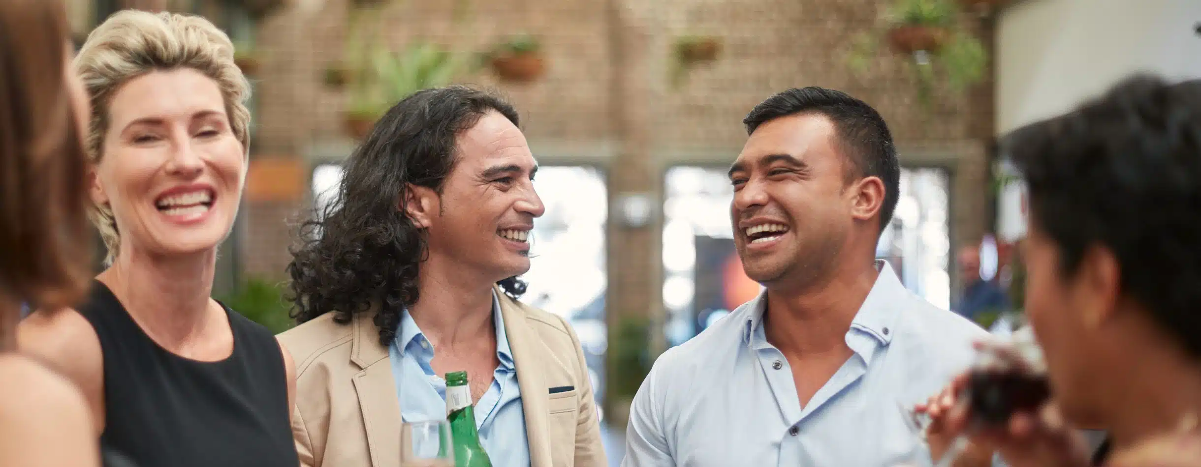 A women, a man with long hair, and another man all dressed in business casual attire share a laugh and a drink at an event.
