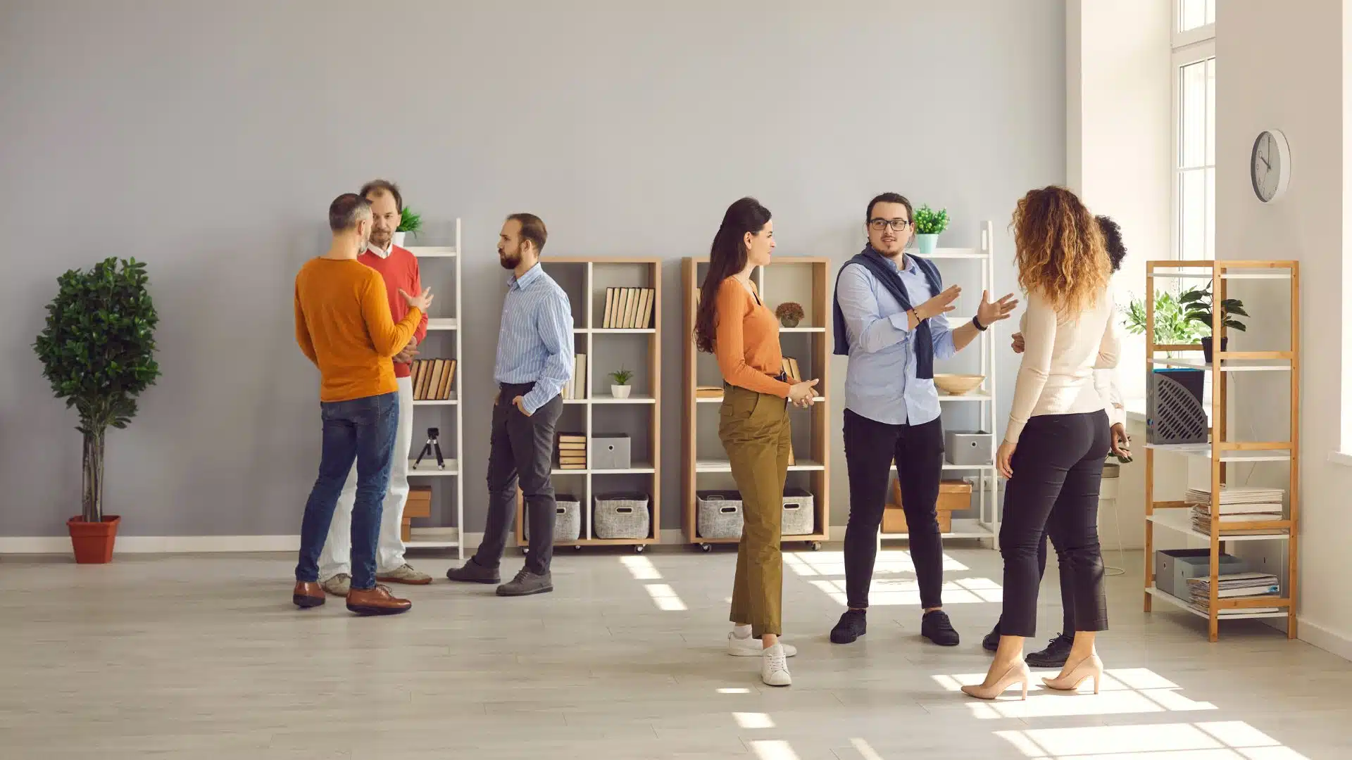 A group of people are participating in one-off conversations between one another in a grey, modern room with adequate natural lighting.