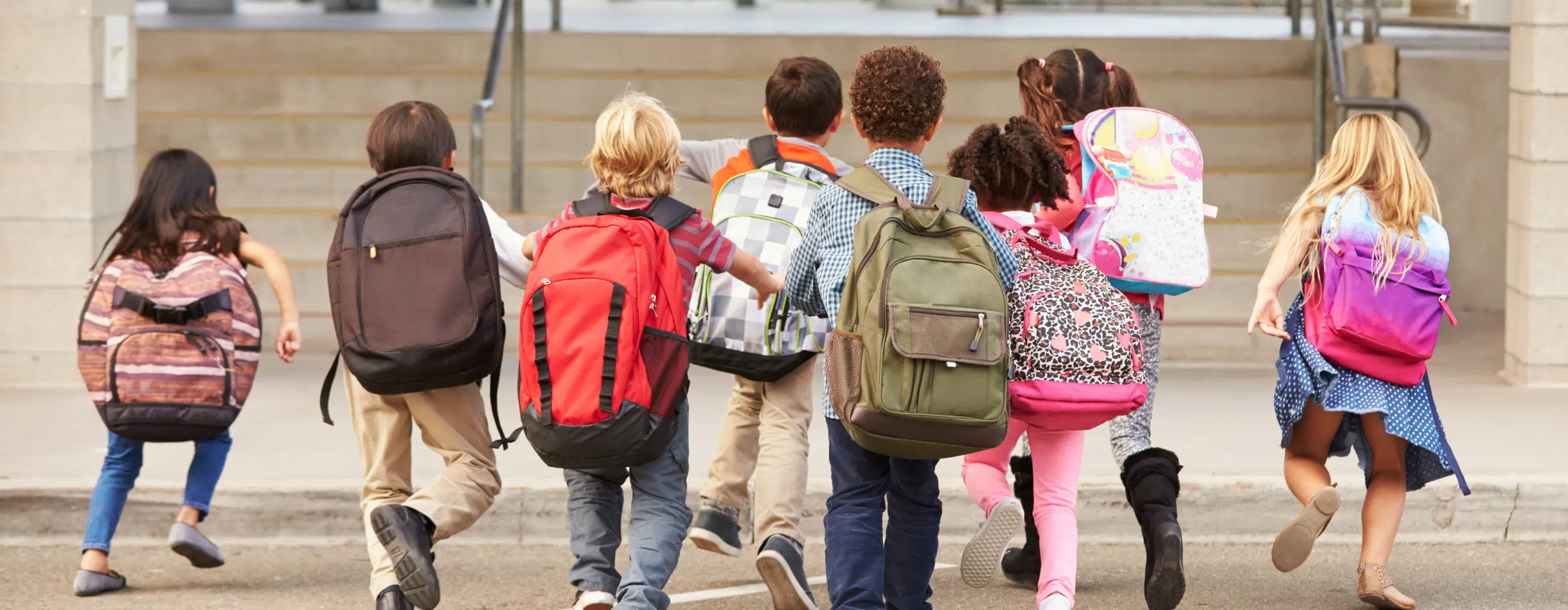 A group of school children with large backpacks heads into a classroom.
